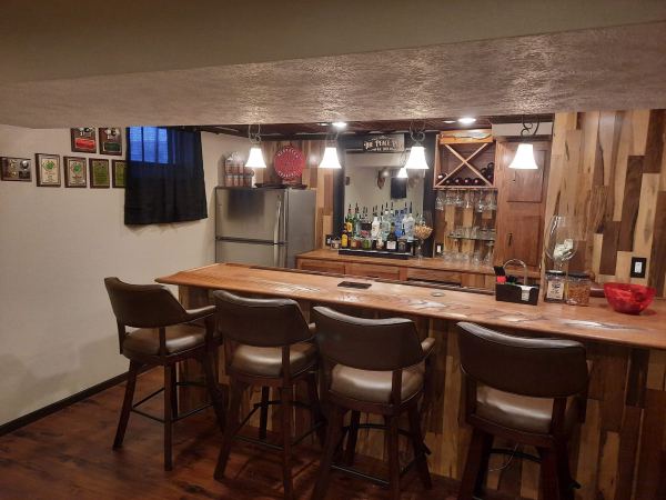 Finished basement bar with custom wood bar top, wood plank wall, and shelving