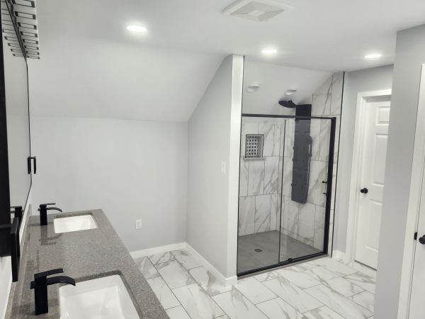 Remodeled bathroom with glass walk-in shower, marble-look tile, and double vanity