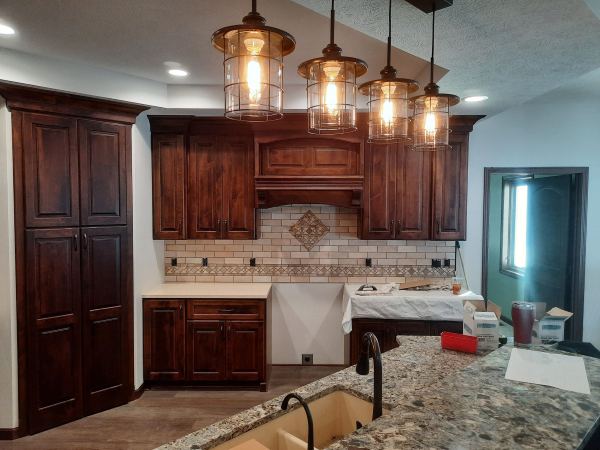 Kitchen with dark wood cabinets, tile backsplash, pendant lights, and granite island