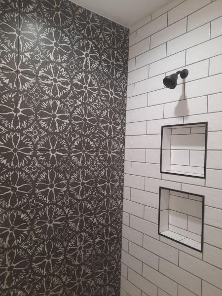 Tiled shower with patterned black accent wall, white subway tile, and two built-in niches